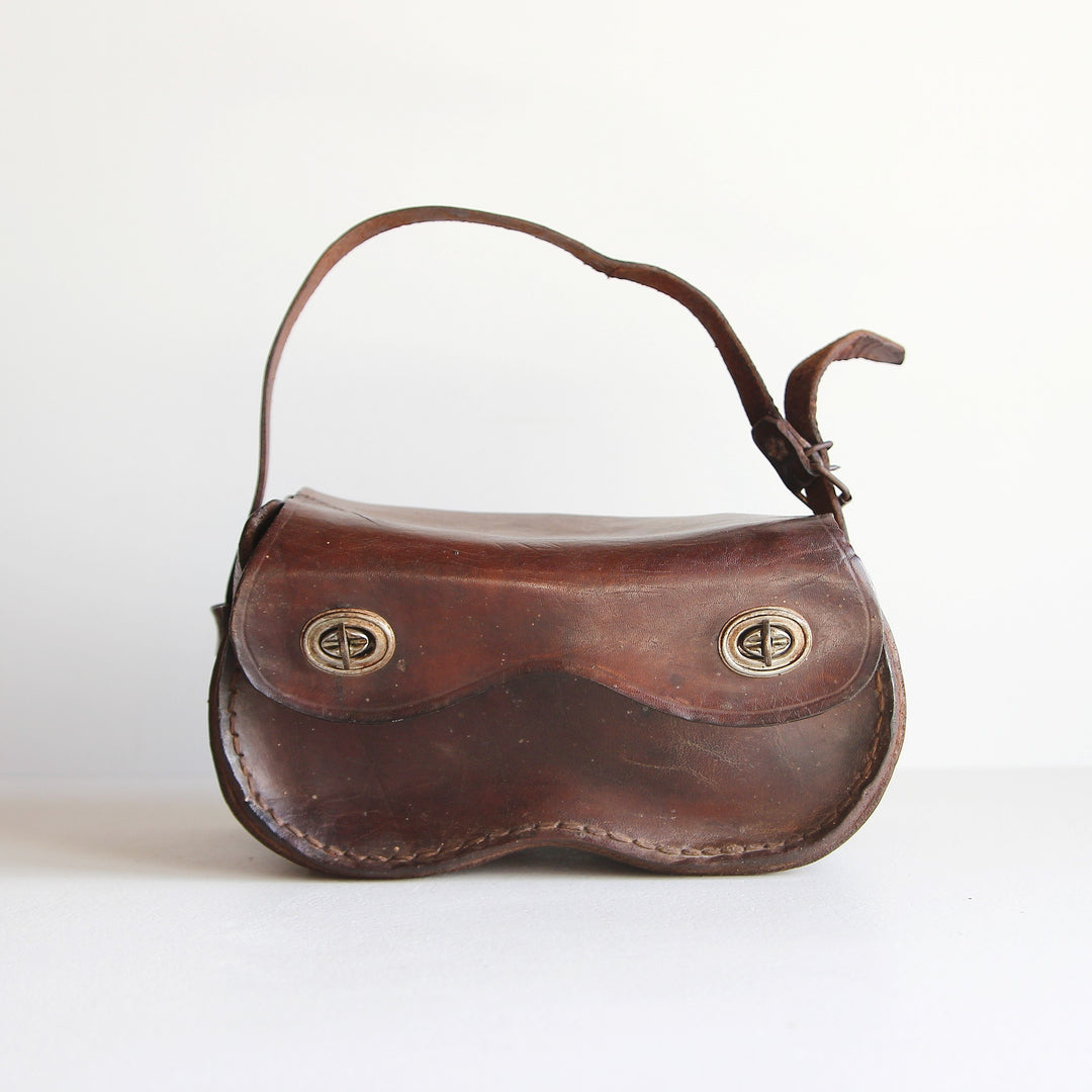 Alte französische Bouletasche aus dunkelbraunem Leder mit zwei ovalen Drehverschlüssen, geschwungener Unterseite und verstellbarem Trageriemen.