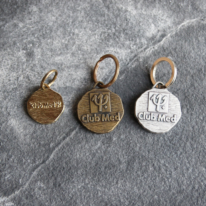Drei alte Club Med Medaillen mit Schlüsselringen: zwei große Ausführungen mit Dreizack-Logo in Bronze- und Silberoptik sowie eine kleine bronzefarbene Medaille.