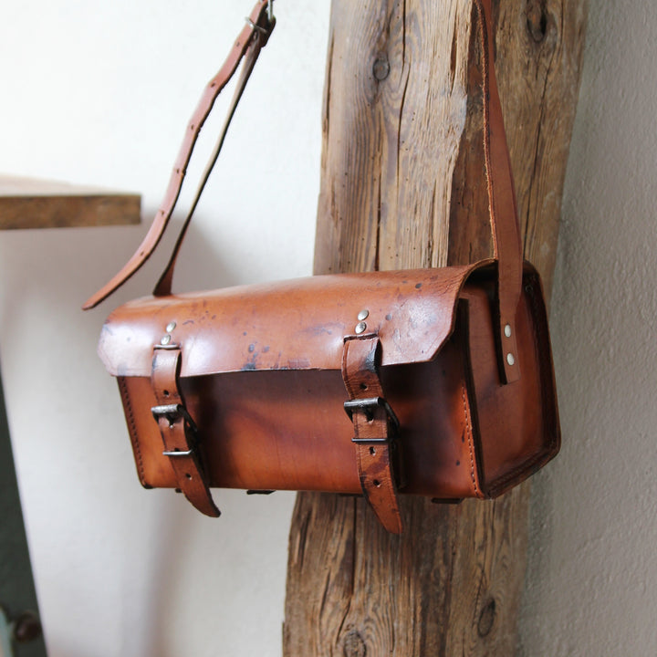 Alte französische Klempnertasche aus braunem Leder mit Schulterriemen und zwei Schnallen.