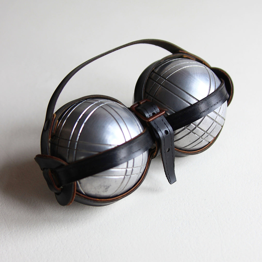 Französisches Petite-Boule-Set mit zwei silberfarbenen Metallkugeln mit Linienmustern und schwarzem Lederhalter mit Schnallen.