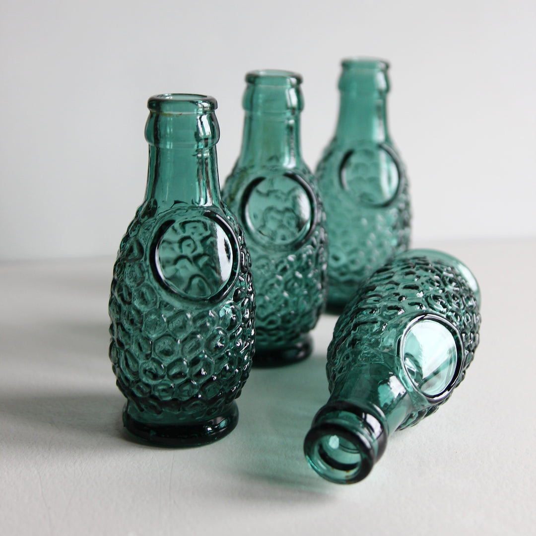 Kleine türkisgrüne Glasvase aus einer alten französischen Saftflasche mit wabenförmigem Reliefmuster und rundem Feld auf der Vorderseite.