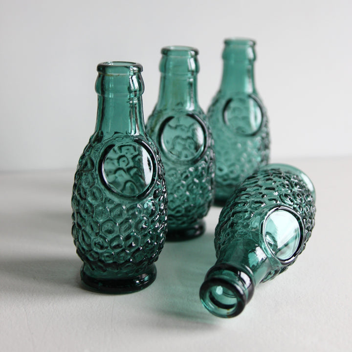 Kleine türkisgrüne Glasvase aus einer alten französischen Saftflasche mit wabenförmigem Reliefmuster und rundem Feld auf der Vorderseite.