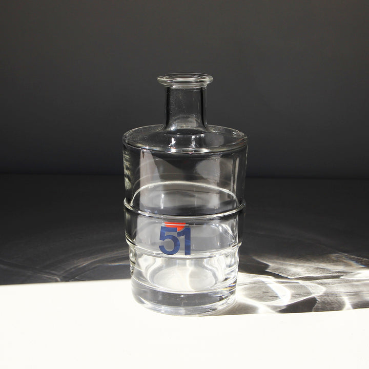 Runde Pastis 51 Wasserkaraffe aus klarem Glas mit blau-rotem 51-Logo, drei umlaufenden Ringen und schmalem Flaschenhals.