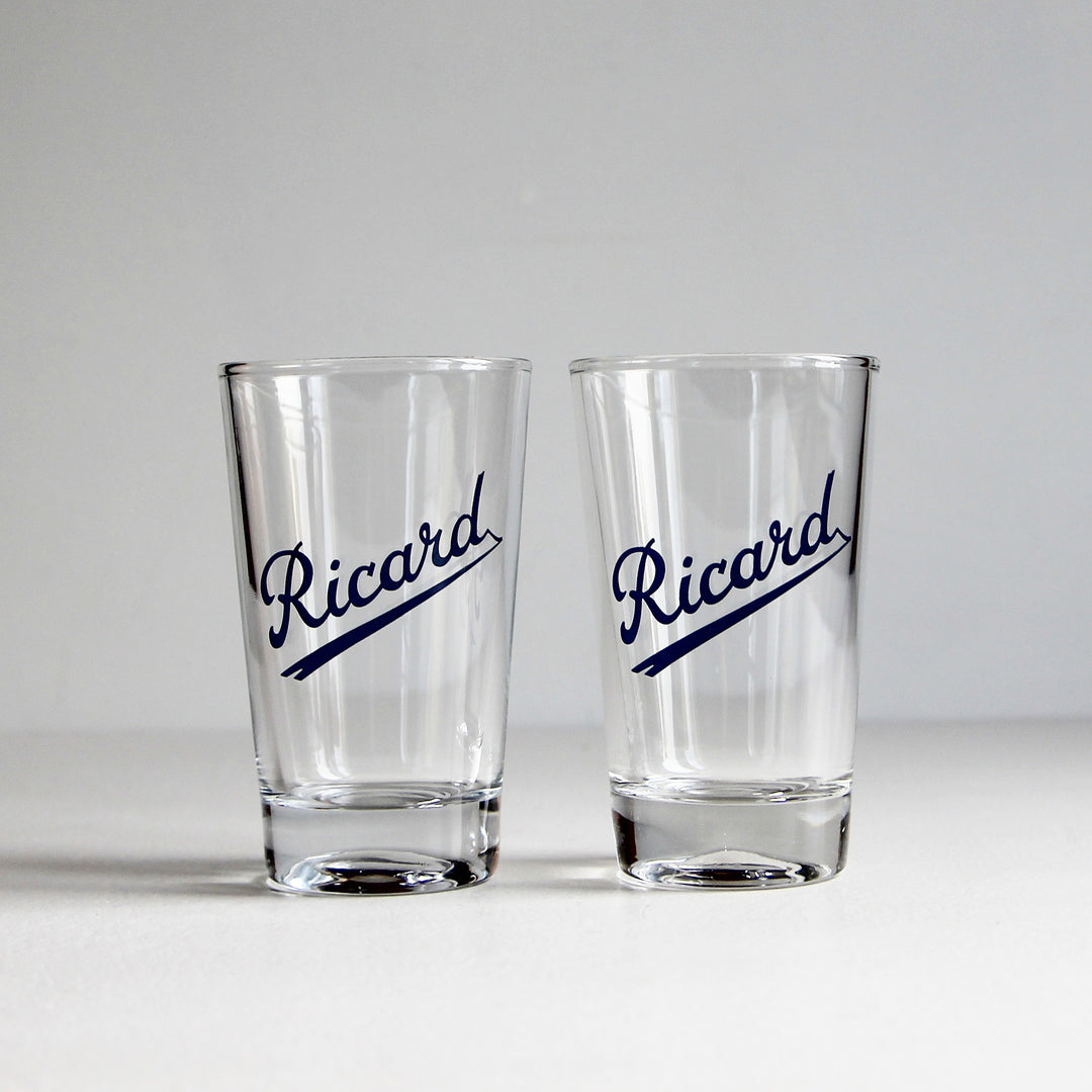 Zwei klare Vintage-Ricard-Pastis-Gläser mit dunkelblauem, diagonal unterstrichenem Schriftzug und massivem Glasboden.