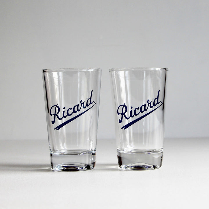 Zwei klare Vintage-Ricard-Pastis-Gläser mit dunkelblauem, diagonal unterstrichenem Schriftzug und massivem Glasboden.