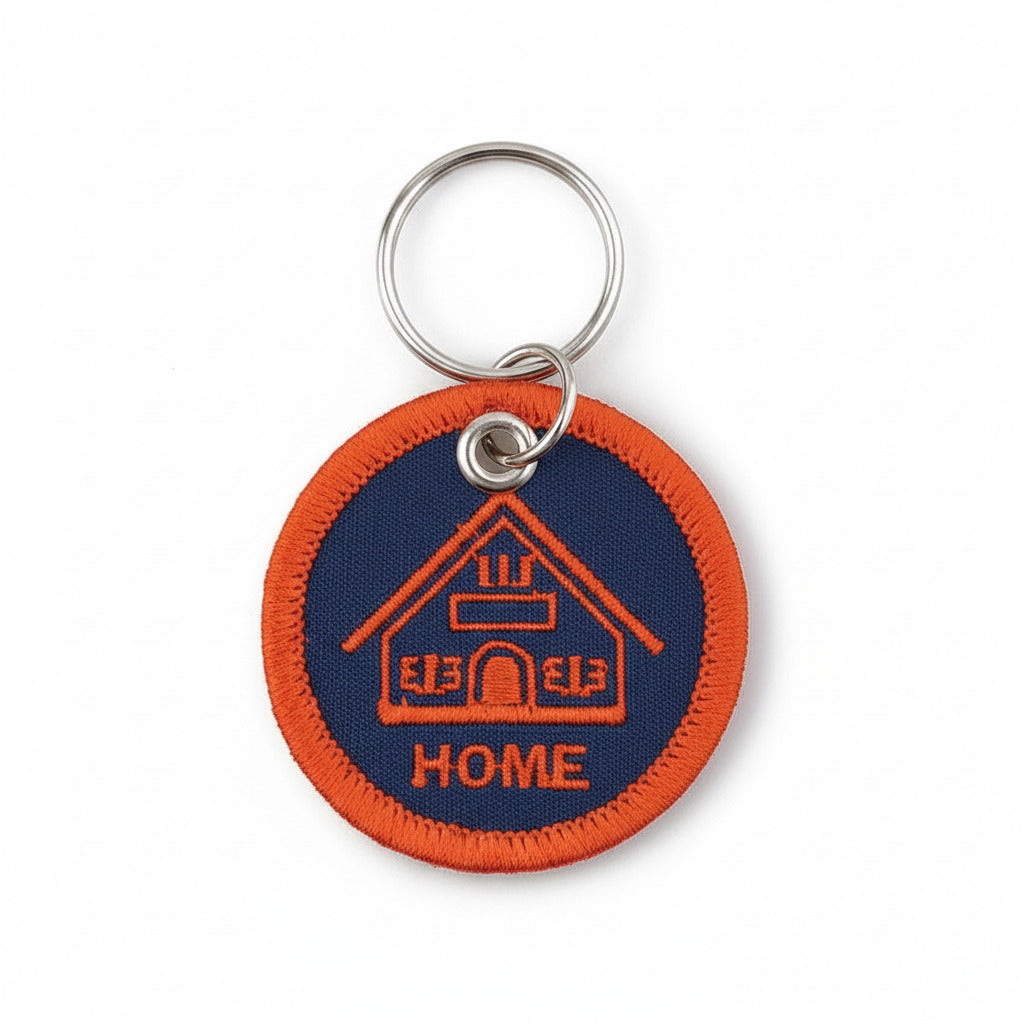 Stitchwork Keychain Home – runder, bestickter Schlüsselanhänger mit Hausmotiv in Dunkelblau und Orange.