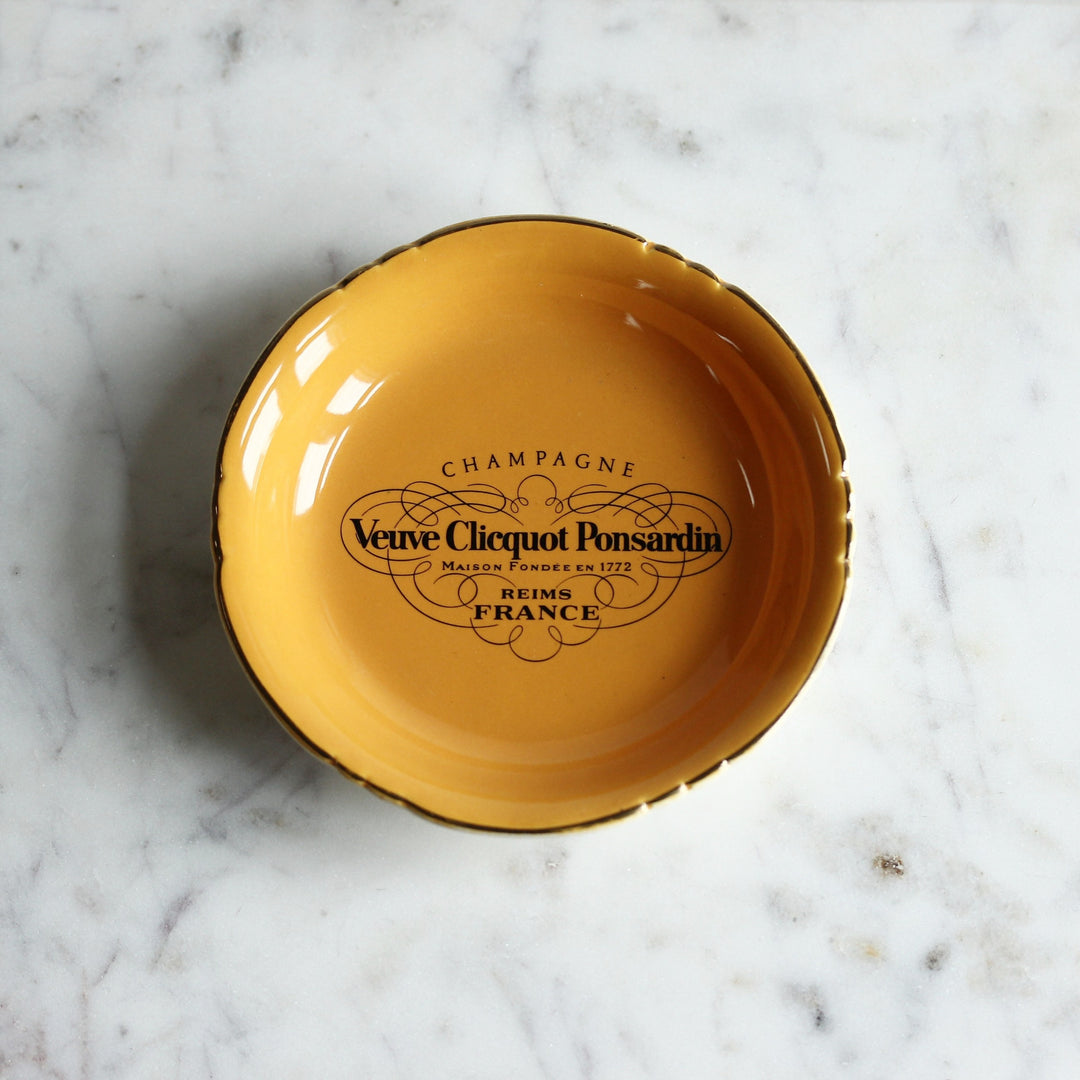 Kleine gelborange Veuve Clicquot Ponsardin Porzellanschale von Villenauxe en Champagne mit schwarzem Champagner-Logo und gewelltem Goldrand.