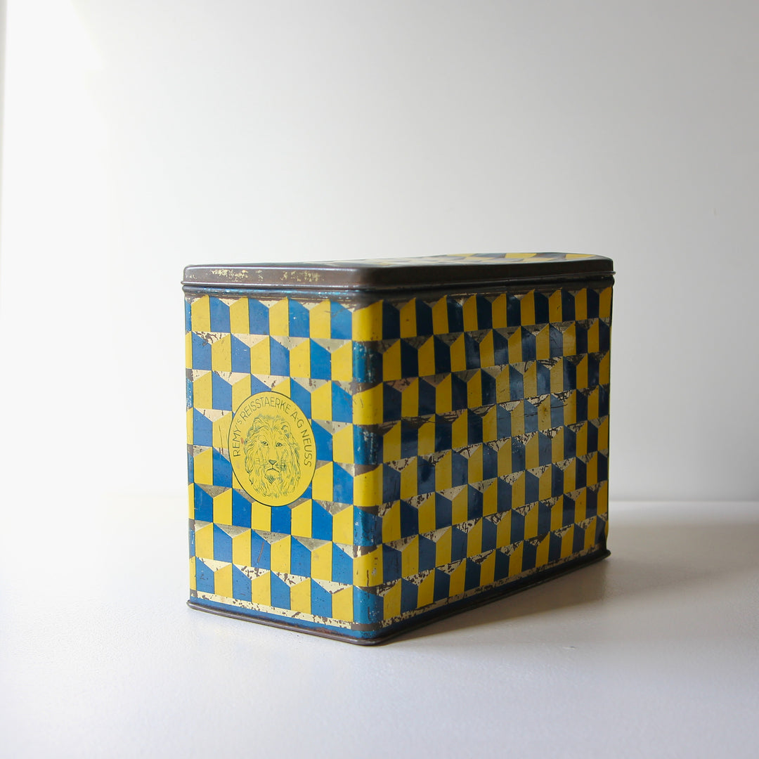 Vintage Blechdose von Remy's Reissstärke Marke Löwenkopf mit blau-gelbem Art-Déco-Würfelmuster aus den 1920er bis 1930er Jahren.
